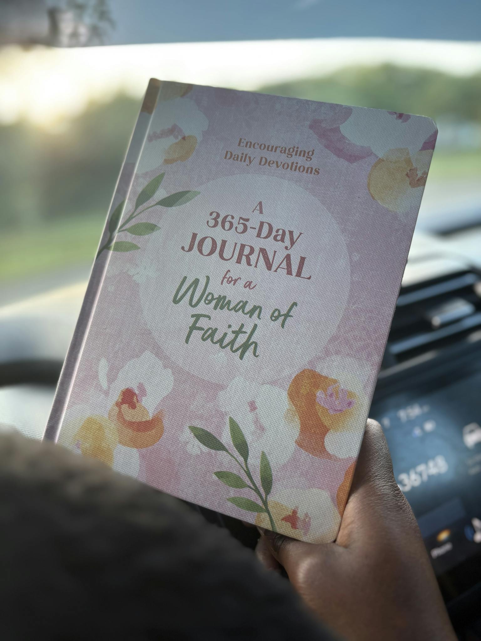 A woman holding a 365-day faith journal while traveling in a car, emphasizing daily devotion.