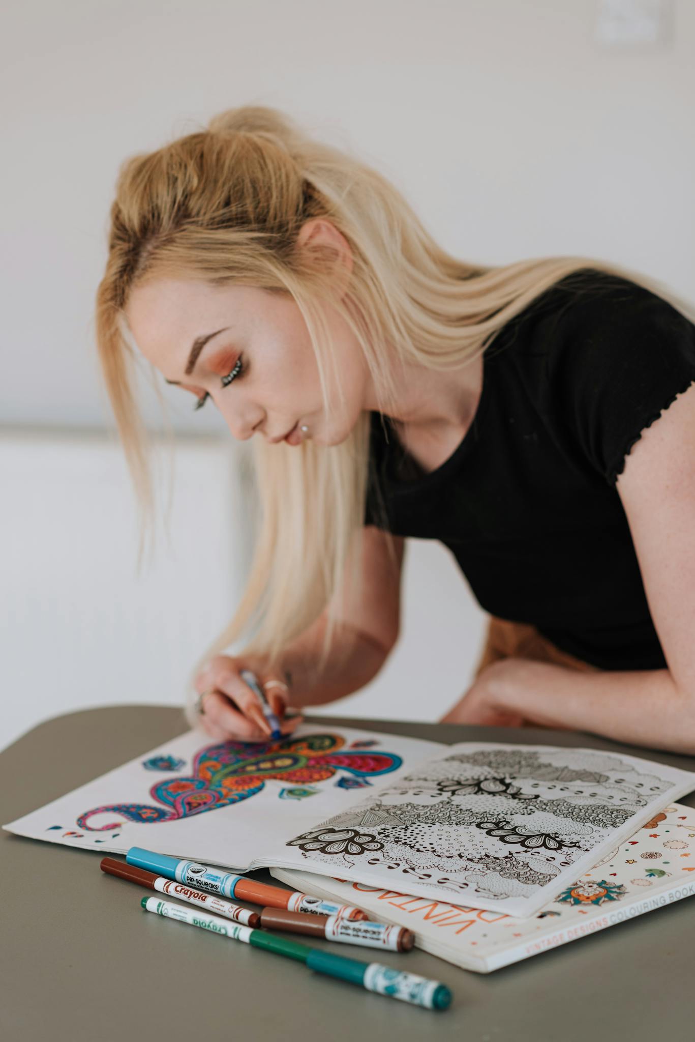 A woman intently coloring an intricate drawing with colorful felt pens, showcasing creativity.